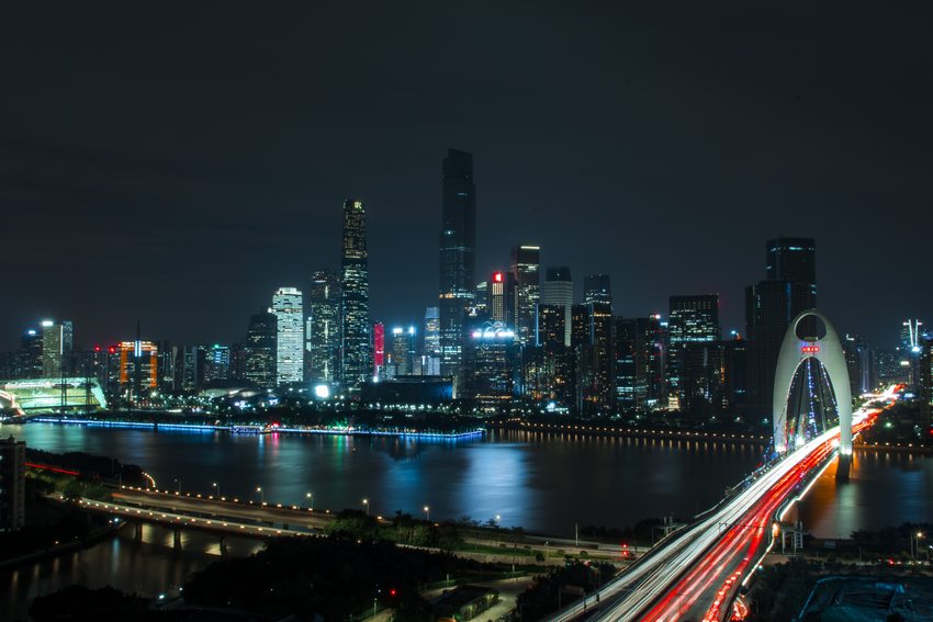 Guangzhou’s illuminated riverfront and traffic light trails crossing a bridge.