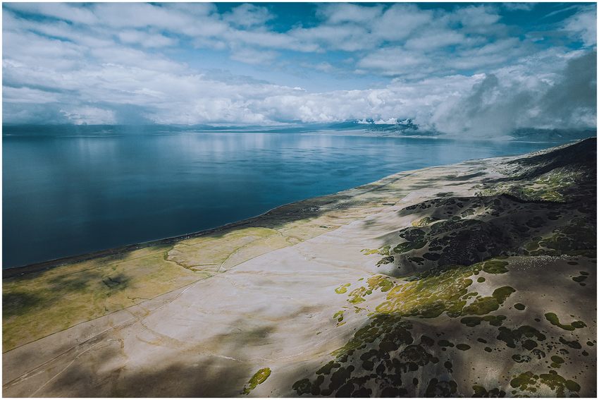 Blue lake water beside pale slopes beneath cloud-filled skies