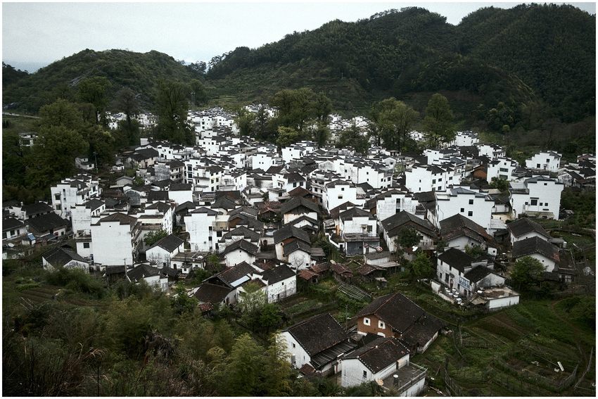 A village of white walls and dark roofs surrounded by green hills