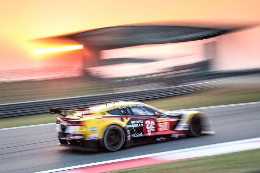 A yellow GT race car speeding along a circuit in the evening light
