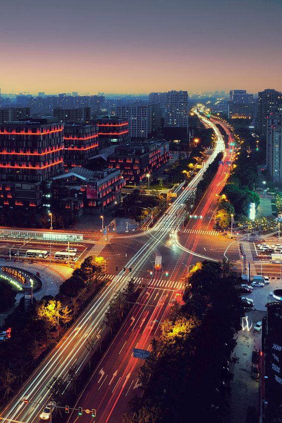 Roads and vehicle light trails running between city buildings at dusk