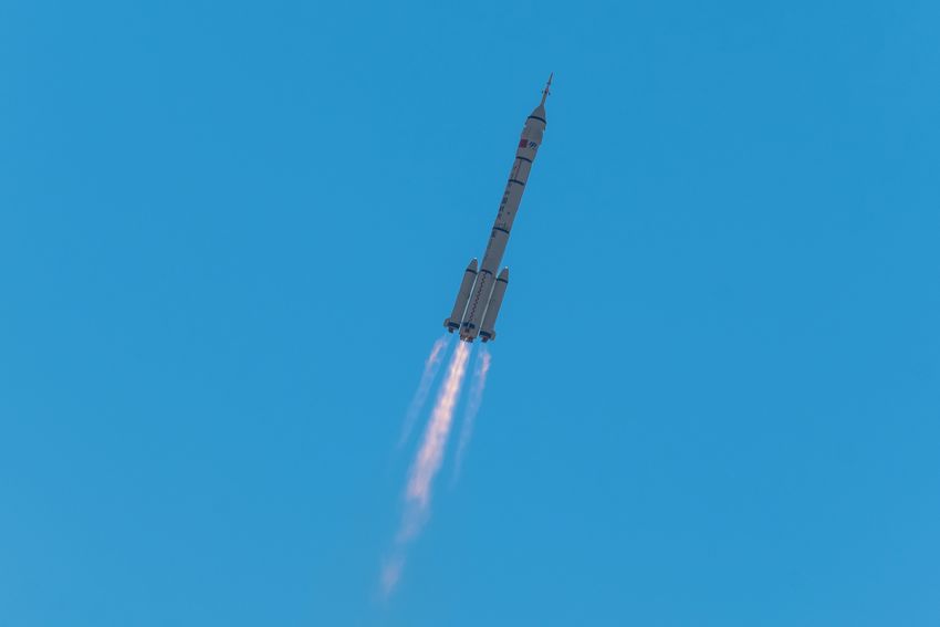 A rocket rising into a clear blue sky with a bright exhaust plume
