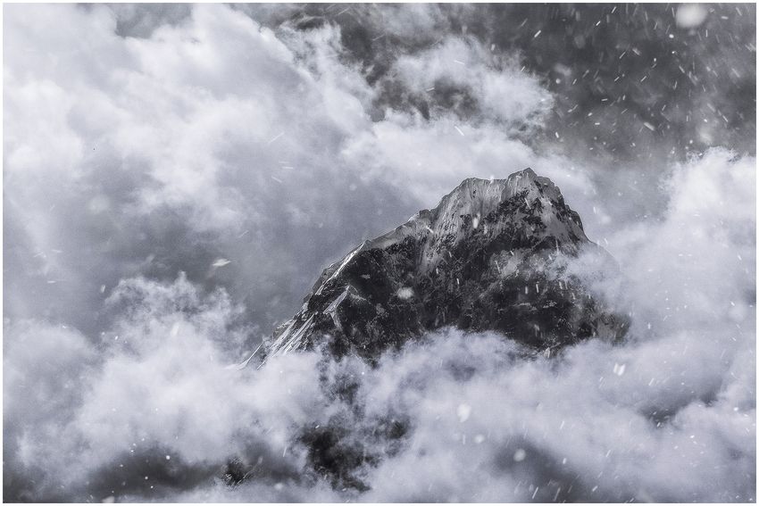 A dark mountain peak surrounded by swirling clouds