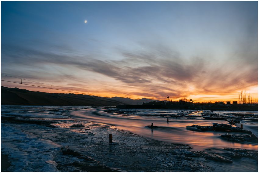 Winding waterways beneath orange twilight and distant hills