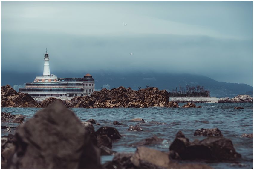 A rocky shoreline with a white tower in the distance
