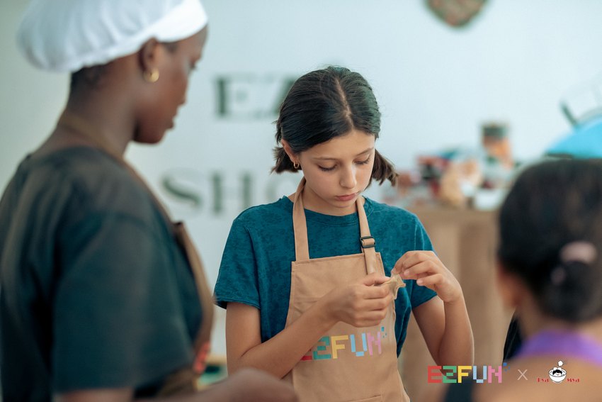 A child concentrates on folding a wonton while an instructor stands nearby.