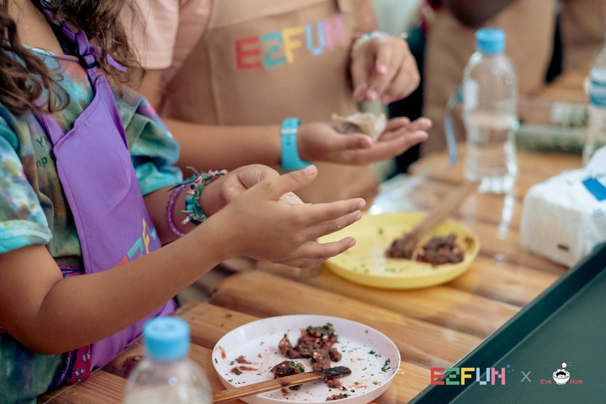 Children shape wontons beside plates of filling and wrappers.
