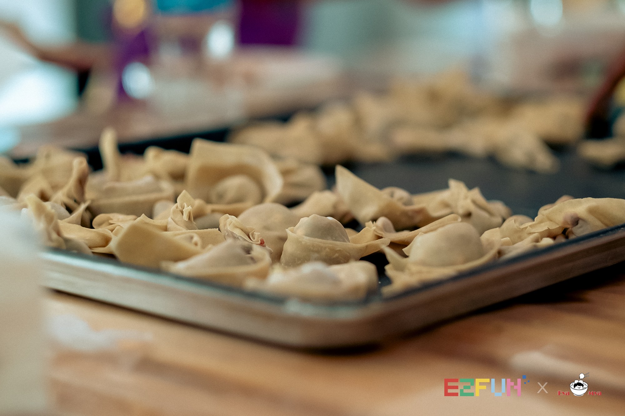 Rows of handmade wontons rest on a metal tray.