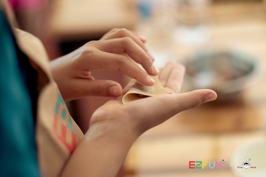 A close view of hands folding a filled wonton wrapper.