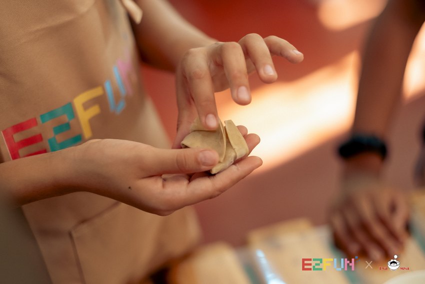 Small hands bring the edges of a wonton wrapper together.