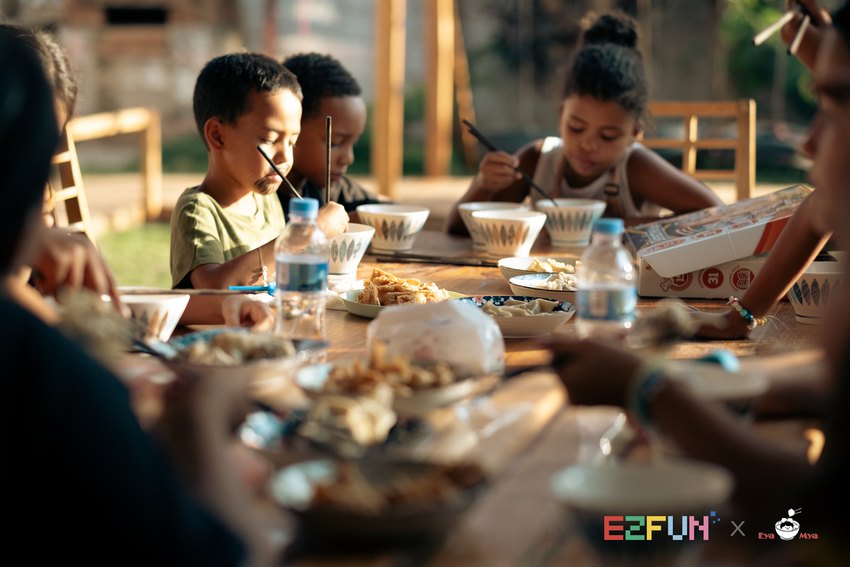 Children enjoy their food together at a sunlit table at EYAMYA.