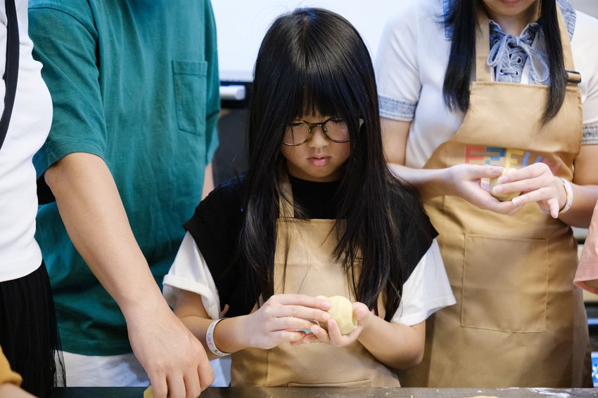 A child carefully shapes a mooncake by hand