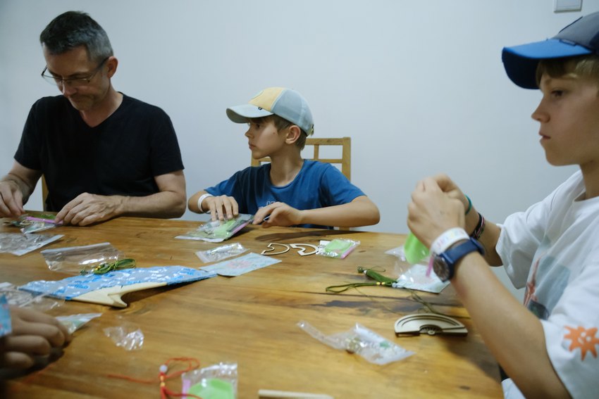 A parent and children work with cords and decorative pieces at the craft workshop