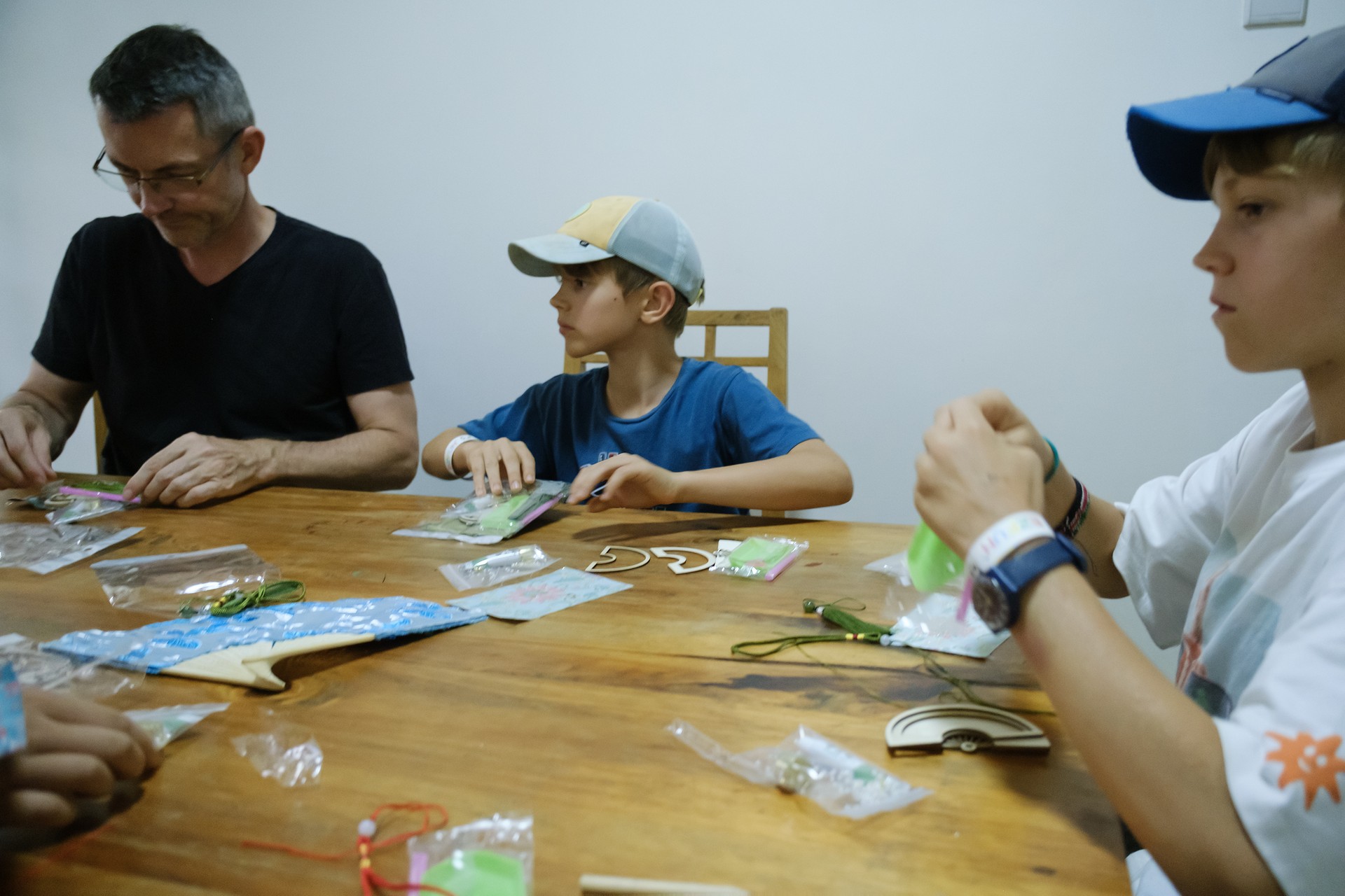 A parent and children work with cords and decorative pieces at the craft workshop