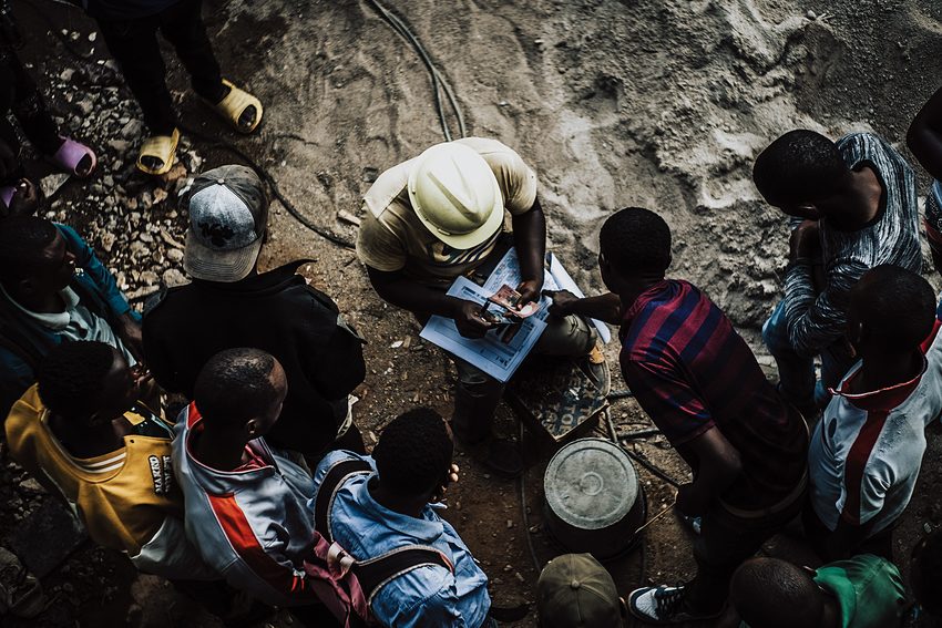 An overhead view shows people gathered around open pages.