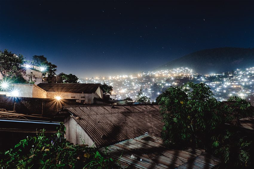 Nearby rooftops and lights on distant hills meet in a night scene.
