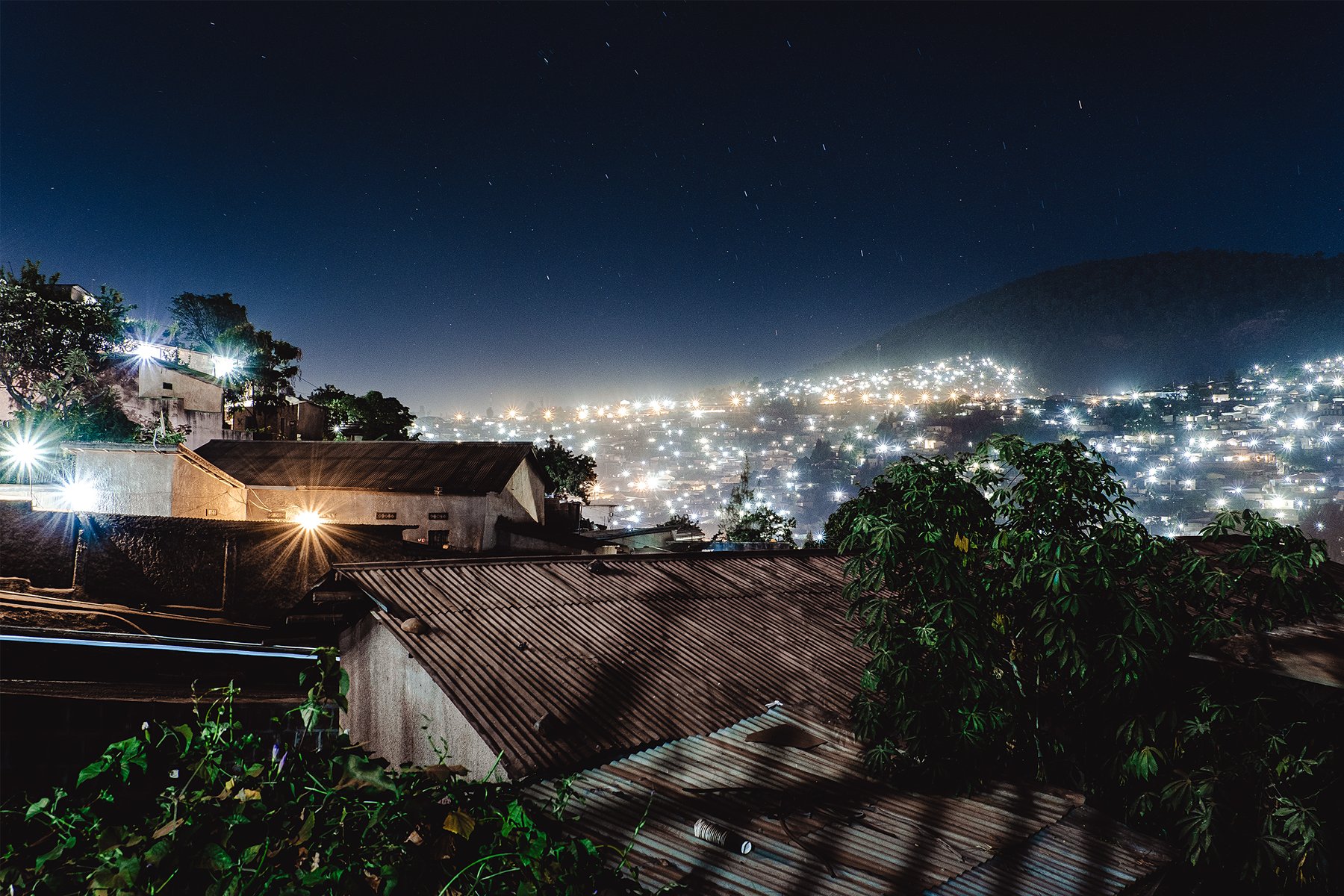 Nearby rooftops and lights on distant hills meet in a night scene.