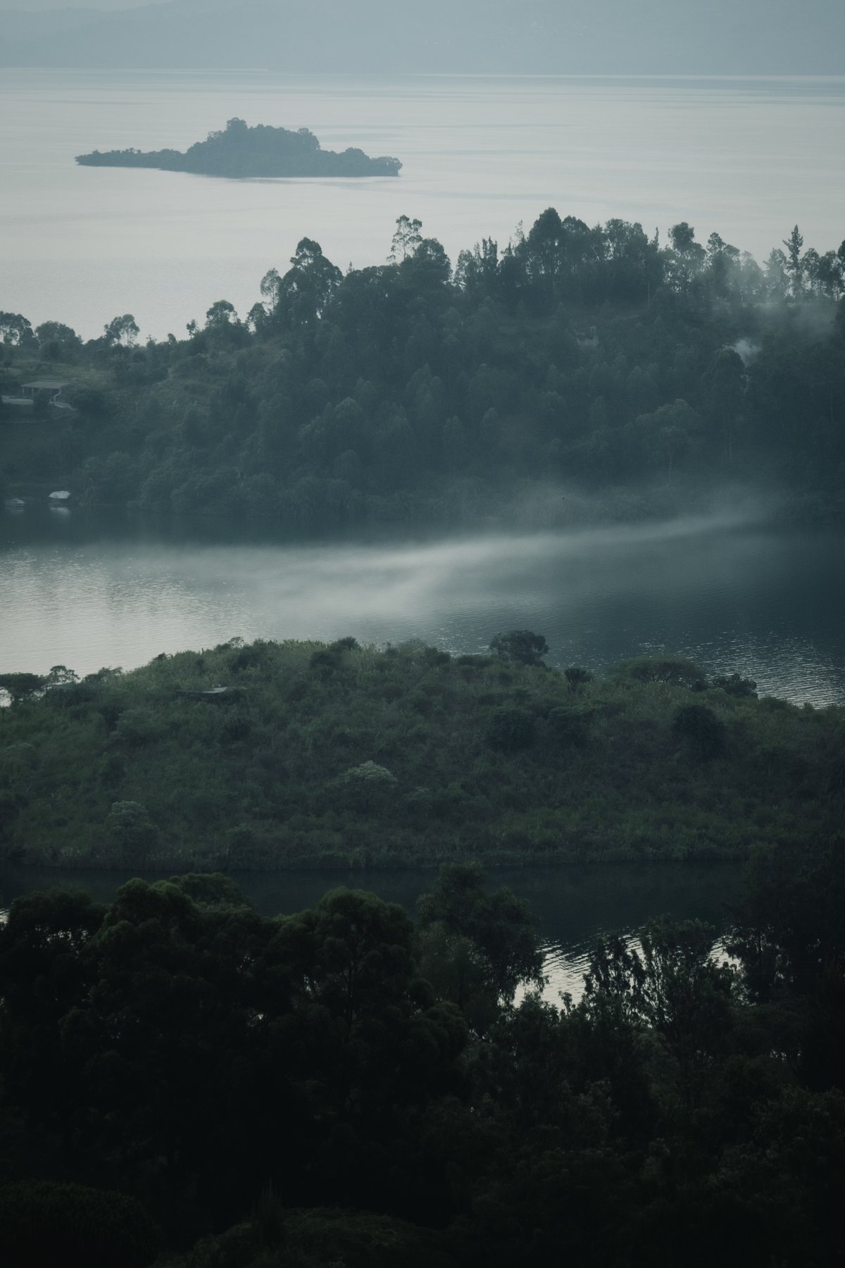 Wooded shores and distant islands sit beneath a pale layer of mist.