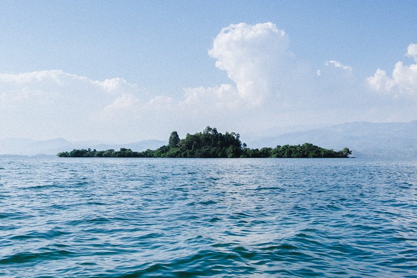 A small wooded island lies in the middle of blue water.
