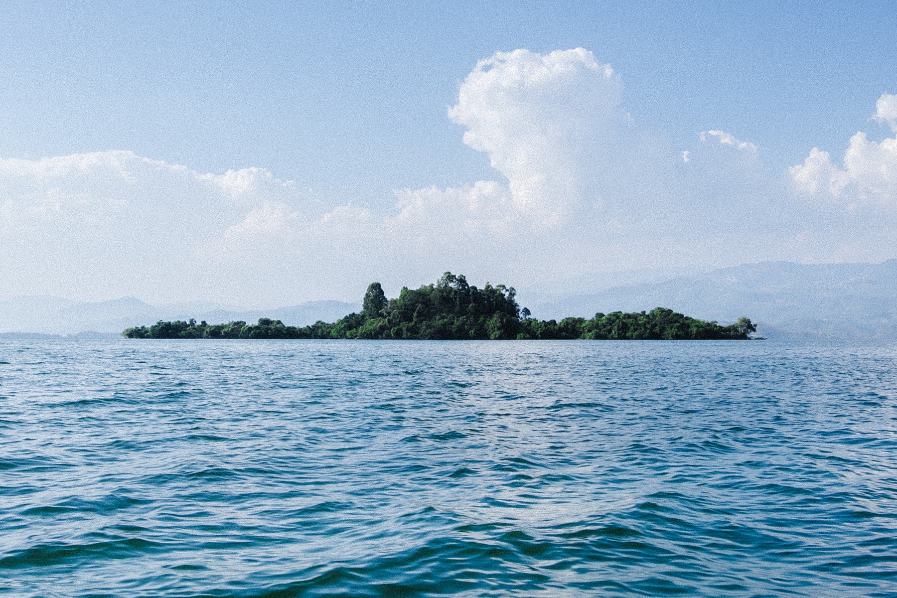 A small wooded island lies in the middle of blue water.