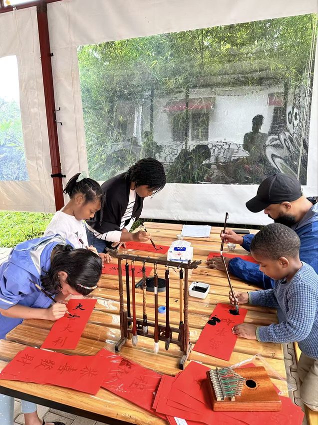 Participants lean over a long table to work with red paper and craft materials.
