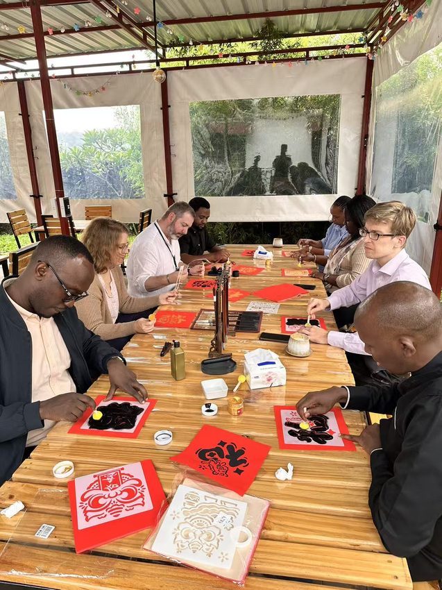 Participants gather around a table scattered with red paper creations and tools.