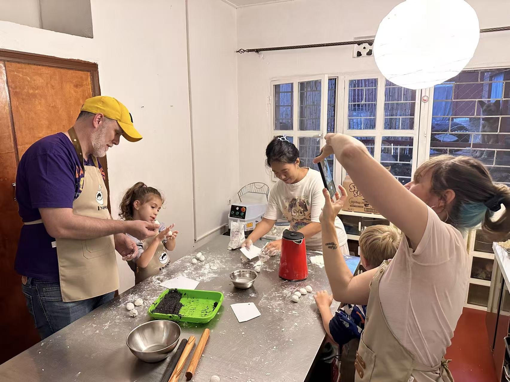 Participants watch and talk around a kitchen worktop with dough-making materials.