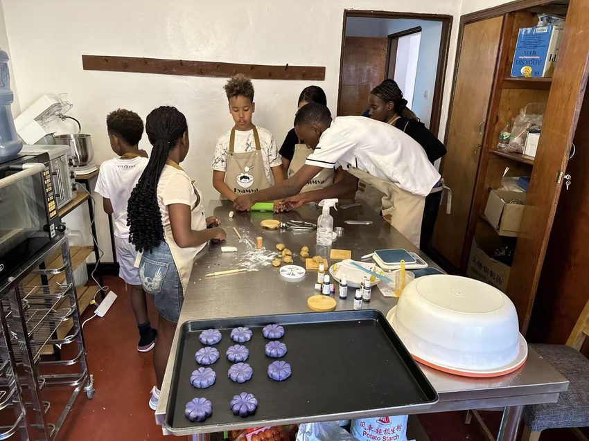 Participants prepare dough-based food together beside a baking tray.