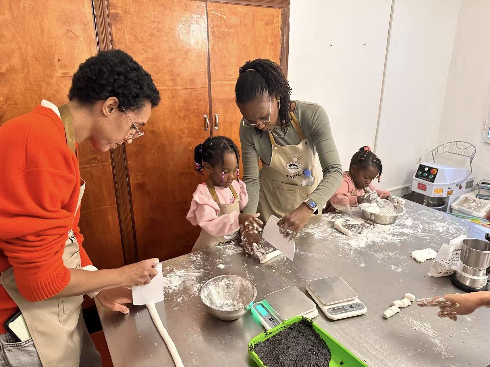 Adults and children press and shape dough on a flour-dusted table.