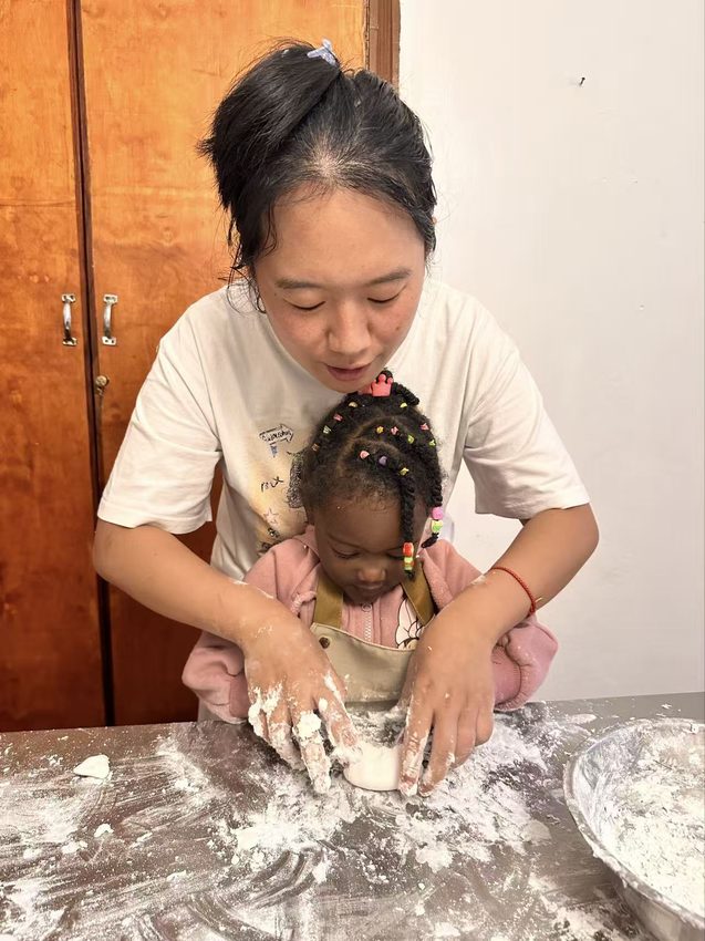 An adult guides a child’s hands at a flour-dusted work surface.